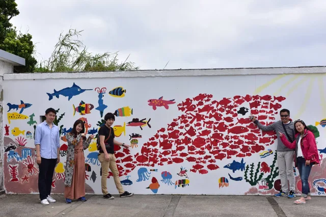 ダイビングツアーの観光で魚の壁画前に集まる参加者