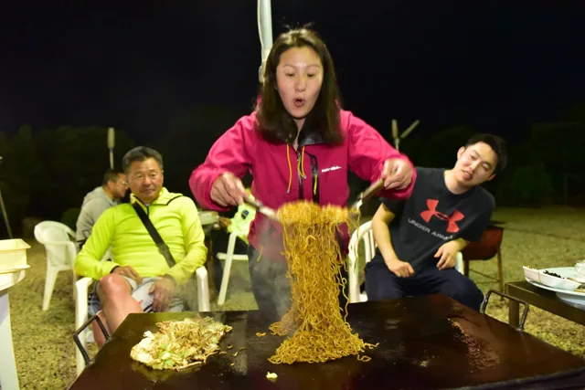 ダイビングツアー中の食事で鉄板の焼きそばを持ち上げる参加者