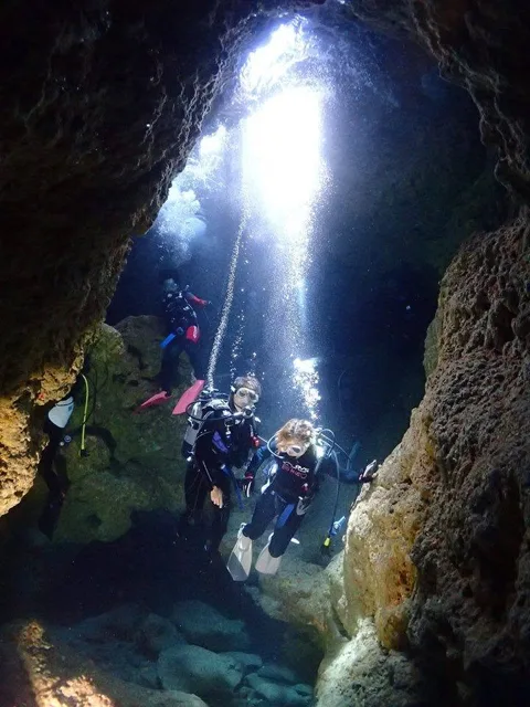 光が差し込む水中の岩場を潜るダイバー