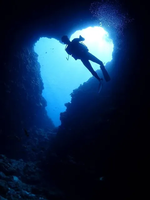 光が差し込む水中の岩場を潜るダイバー