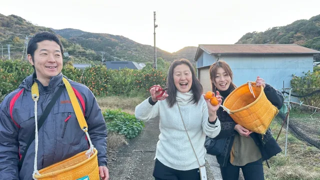 みかんを手に笑顔で記念撮影する3人（ツアー中の観光と推定）