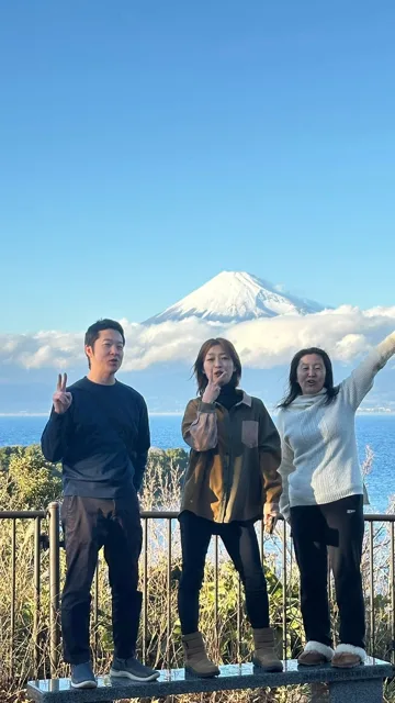 富士山と海を背景に記念撮影する3人（ツアー中と推定）