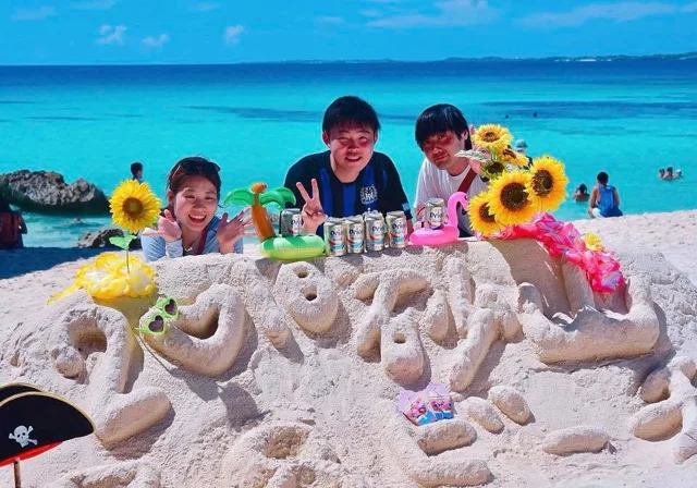 沖縄県・宮古島での宮古島ツアーで青い海と砂の飾りの前に集まった3人の参加者