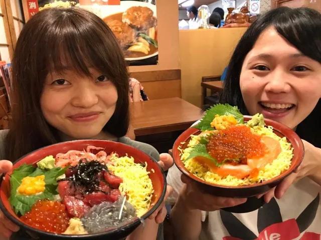 海のツアーの食事で大きな海鮮丼を持つ2人の参加者(元アルバムから推定)