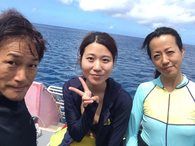 沖縄県・宮古島での宮古島ダイビングツアーで海を背景に記念撮影する3人の参加者