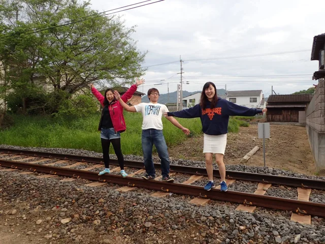 香川県・琴平電鉄沿線（駅名未確認）での四国観光ツアーで琴平電鉄の線路沿いに並ぶ3人の参加者