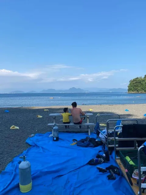 伊豆・大瀬崎（推定）でのダイビング：伊豆の海辺のベンチに座り海を眺める親子。大瀬崎と推定