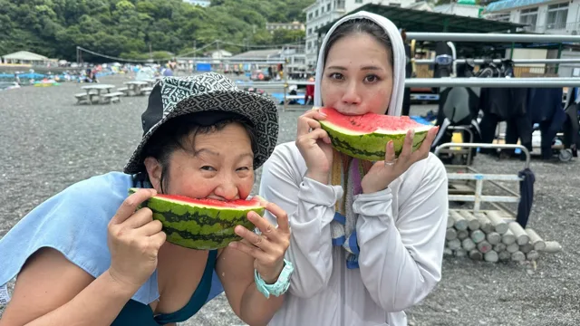 大瀬崎とみられる海岸(景観から推定)での砂利浜の休憩場所でスイカを食べる二人の参加者